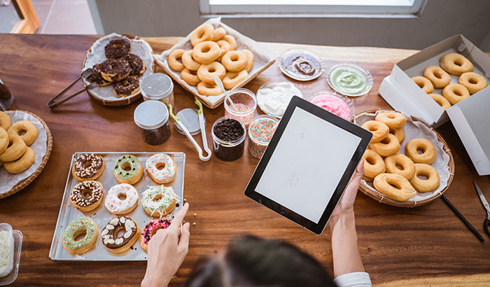 A person holding a tablet with doughnuts and other food.